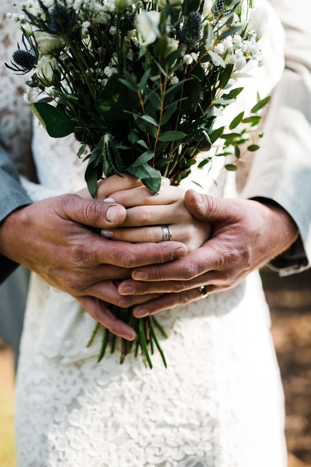 bride and groom holding flowers with rings shining in light