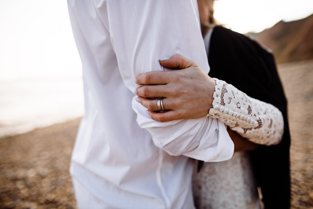 bride holding grooms arms on beach with wedding ring