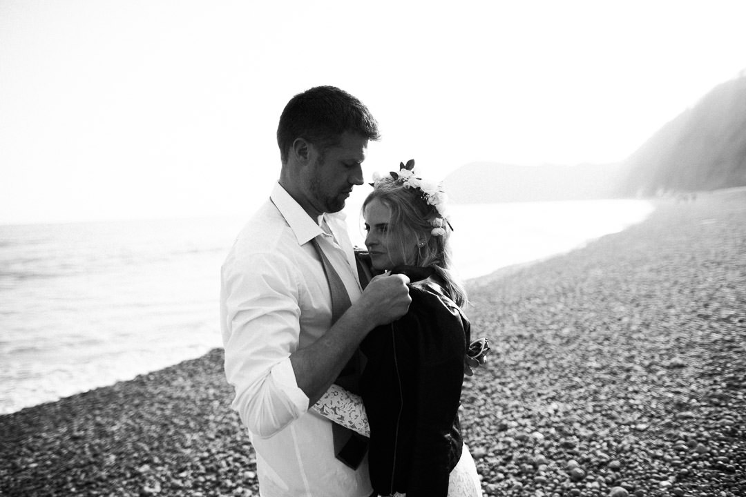 groom putting jacket over brides shoulder on beach