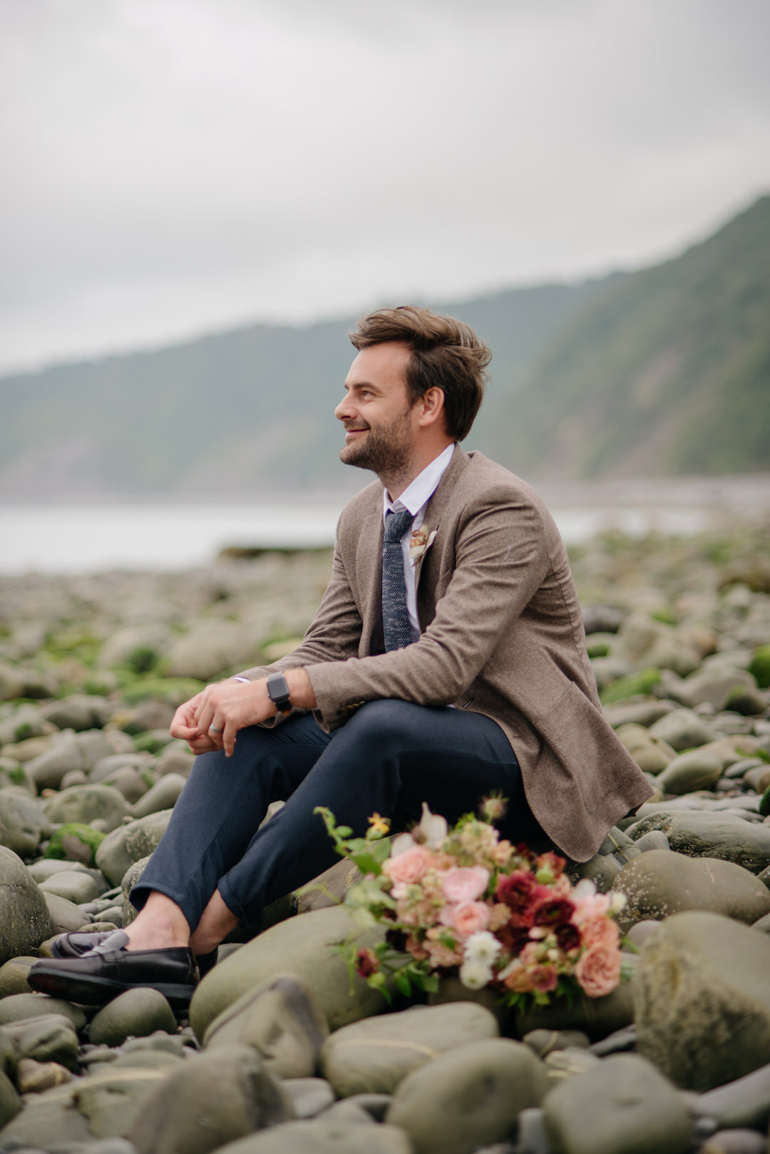 man sat on beach holding wedding flowers