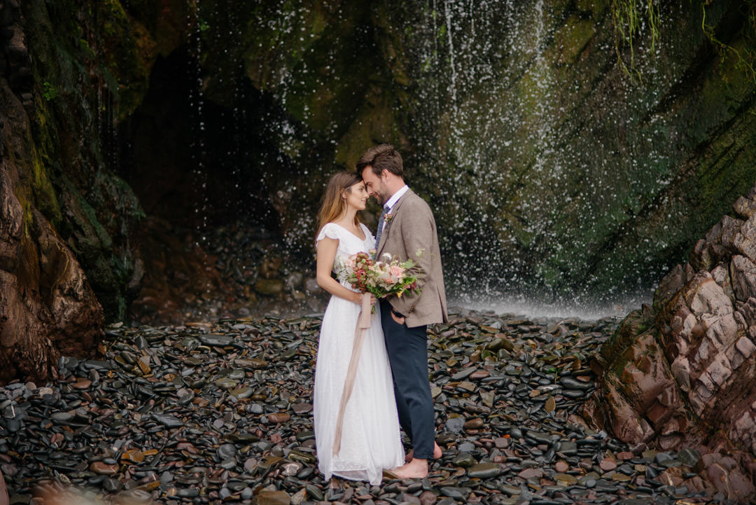 bride and groom stood under waterfall on beach