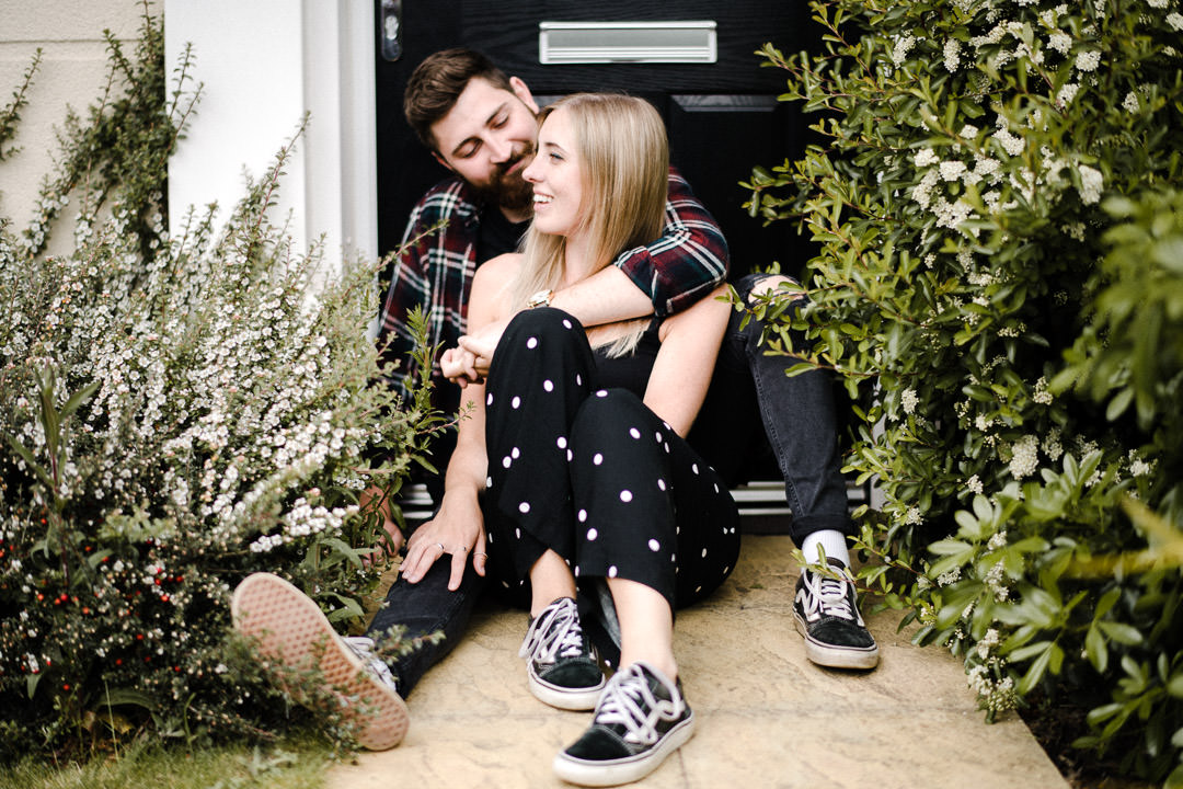 young couple sat smiling on doorstep of house