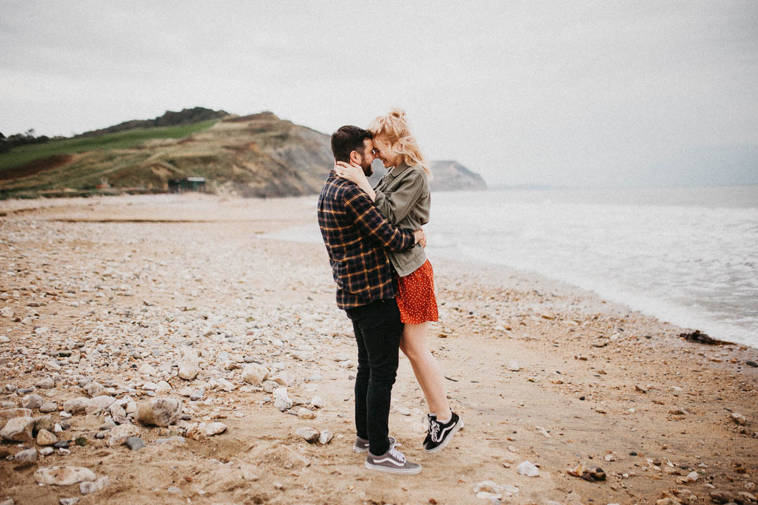 man kissing woman waring orange dress on beach
