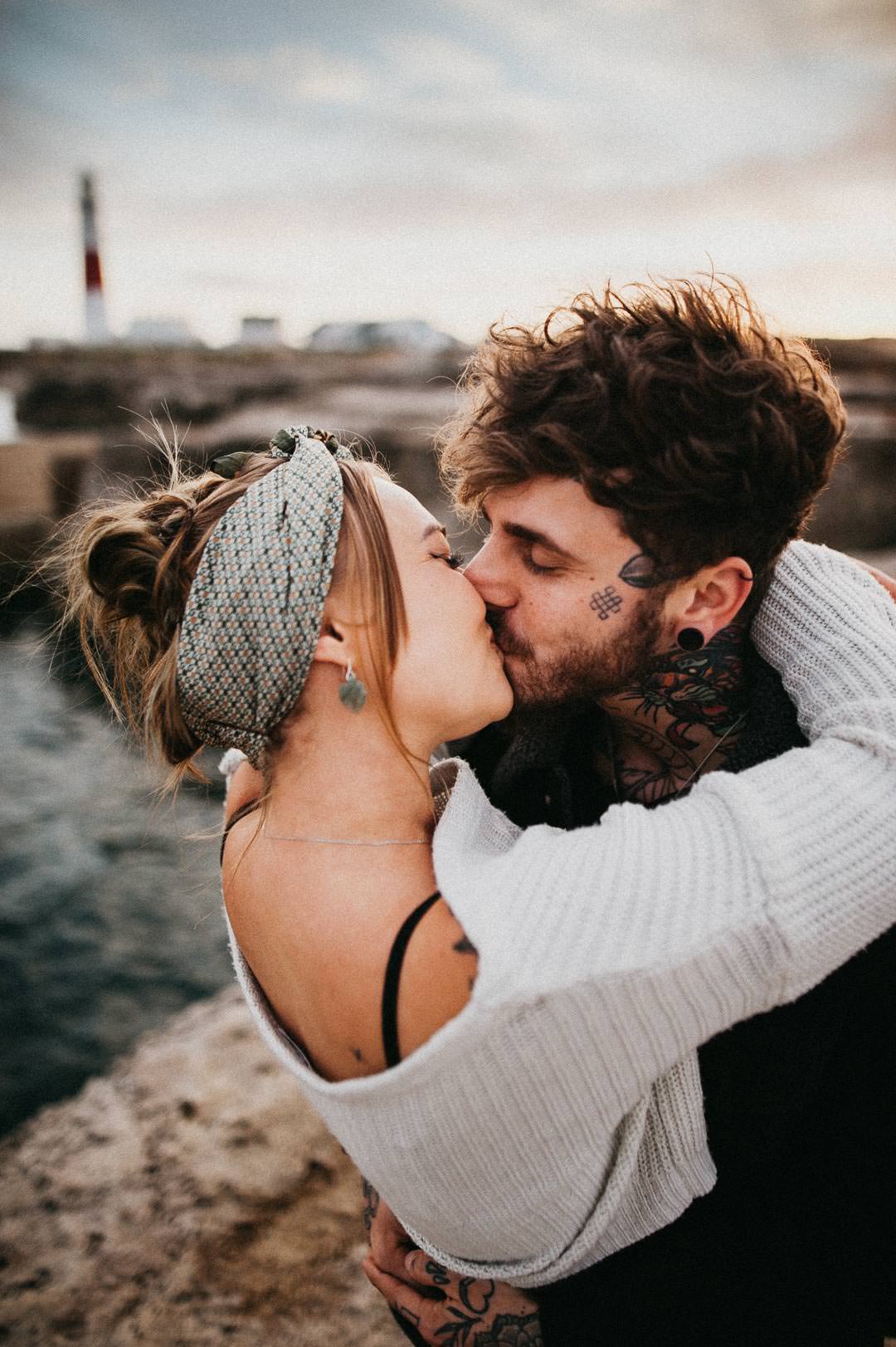 man with tattoos hugging woman in white sweater