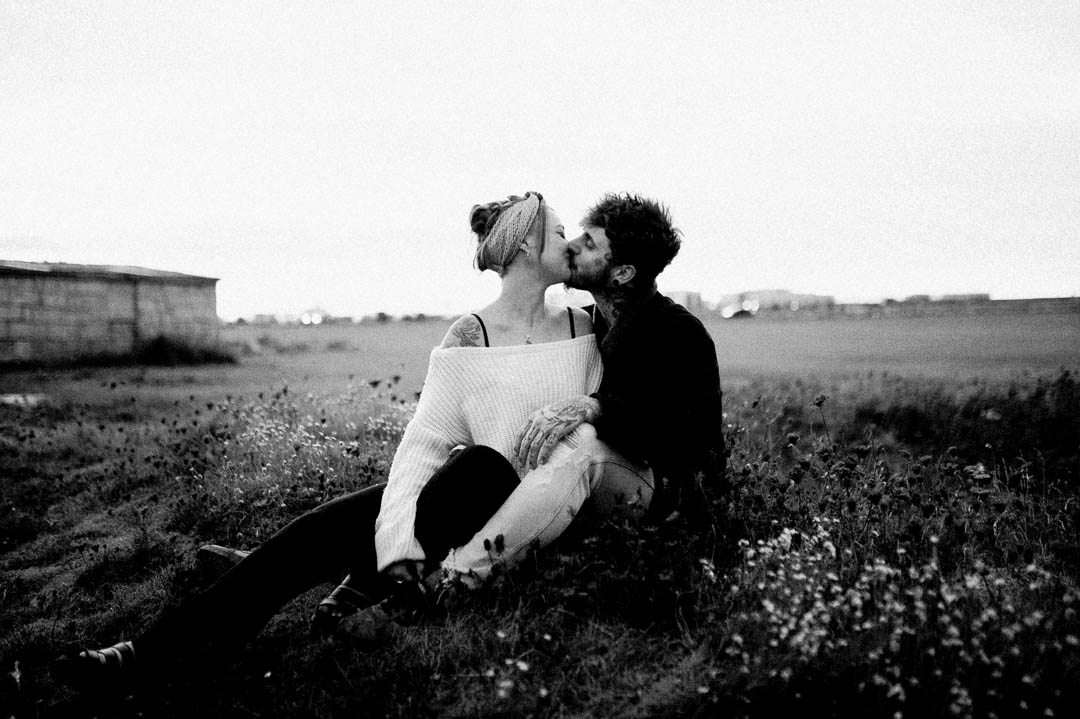 man and woman sat in long grass kissing