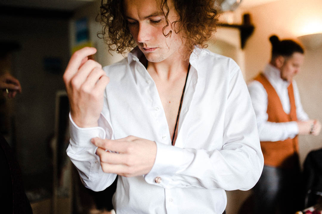 man with long hair putting on white shirt