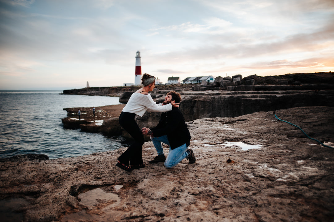 man proposing to woman on rocky beach at sunset