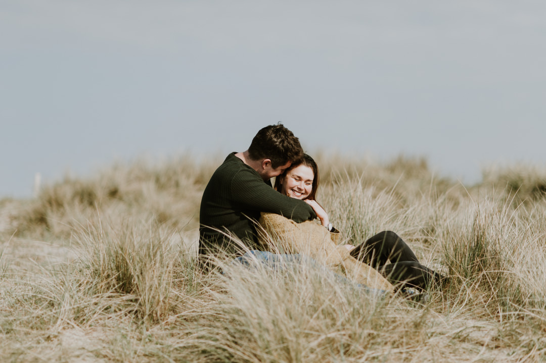 young couple sat in sand dunes smiling