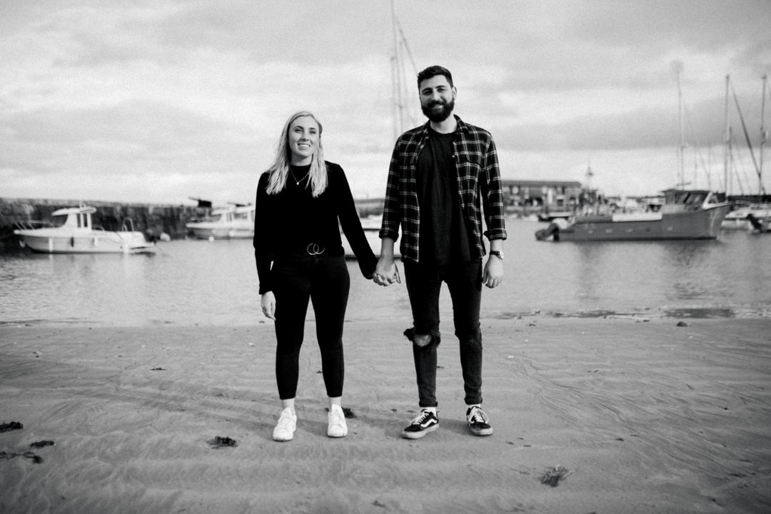 man and woman holding hands on beach near boats