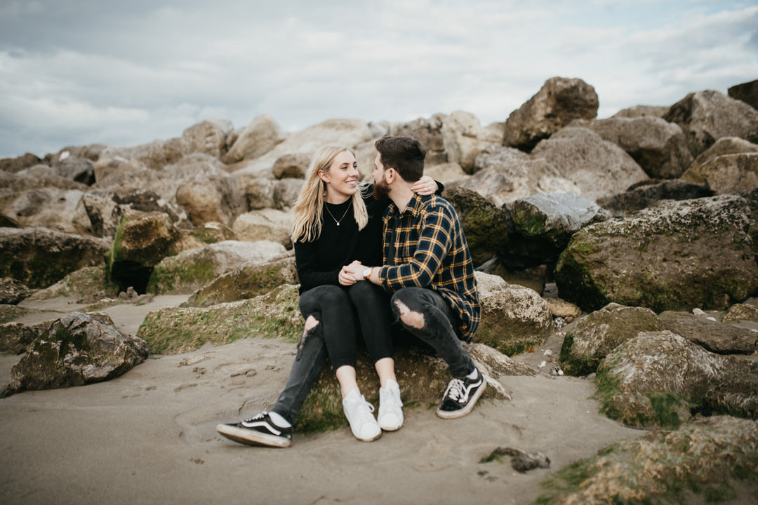 man and woman sat on rocks under grey skies