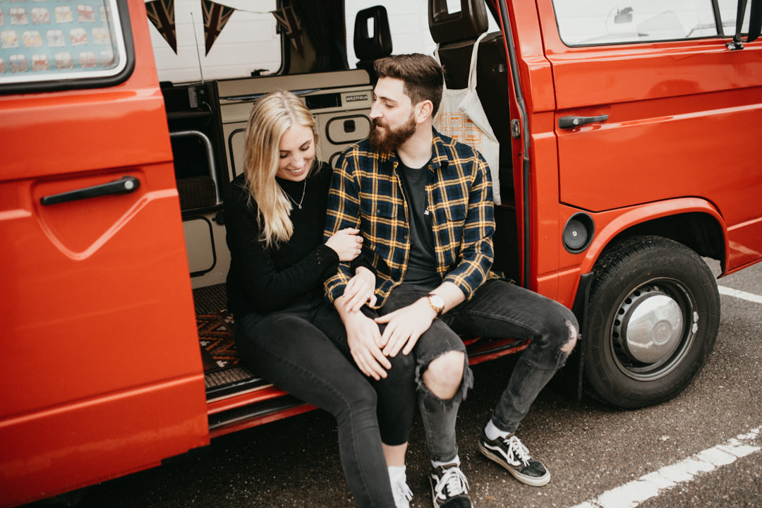 young couple sat in classic camper van near beach