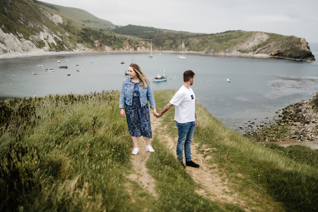 man and woman holding hands on hill near sea