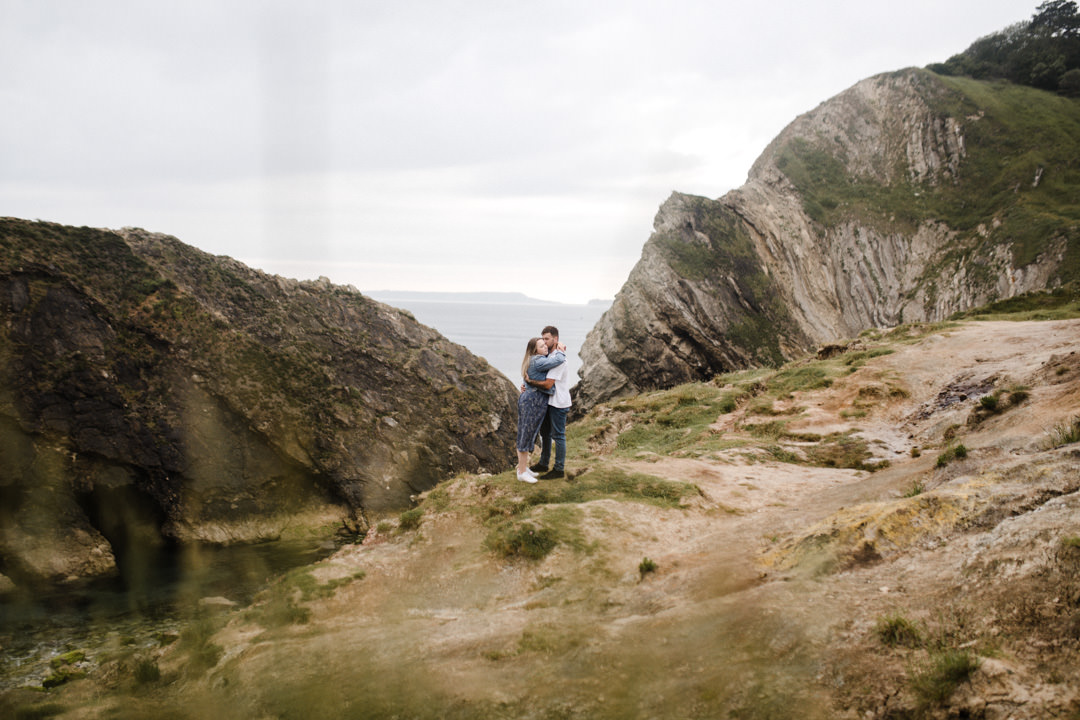 man and woman embracing near rock formation near sea