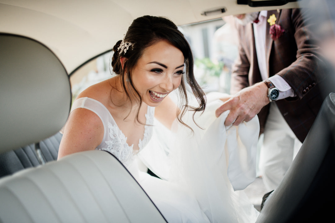 wedding bride getting into classic car holding flowers