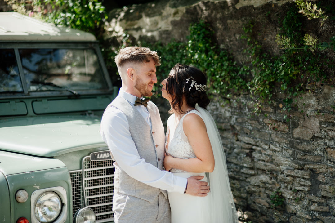 bride and groom stood next to old land-rover car
