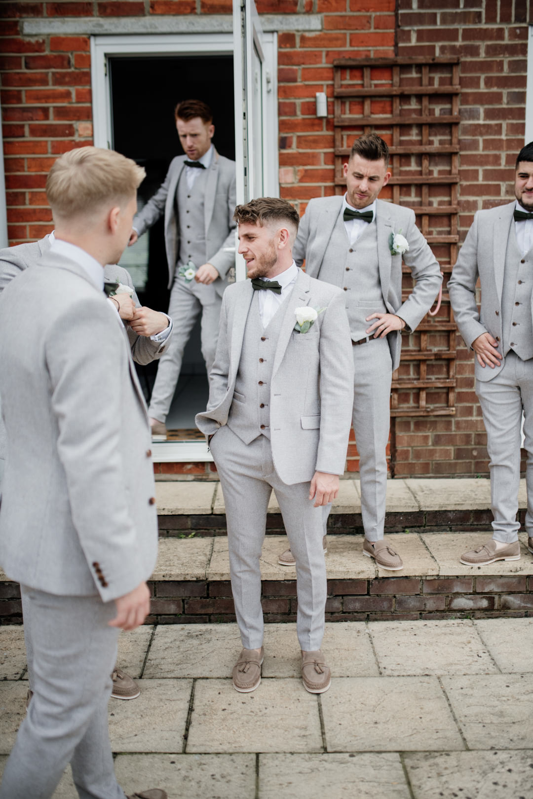 men in grey suits stood outside house laughing