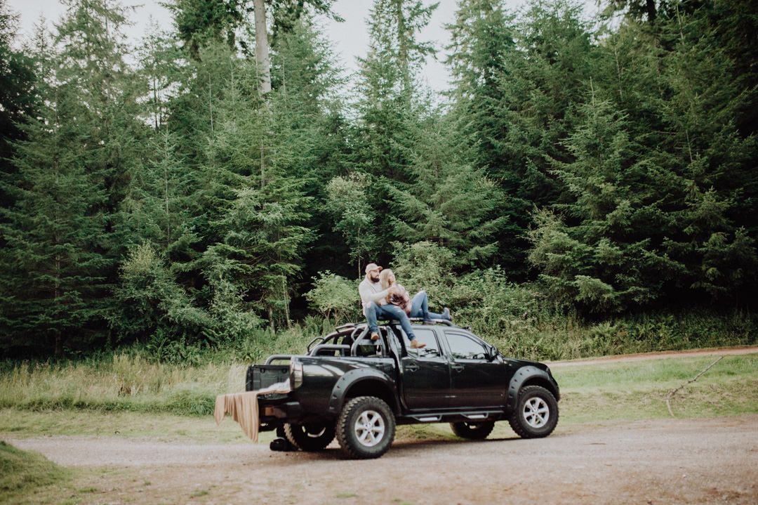 young couple sat on roof of car in woods