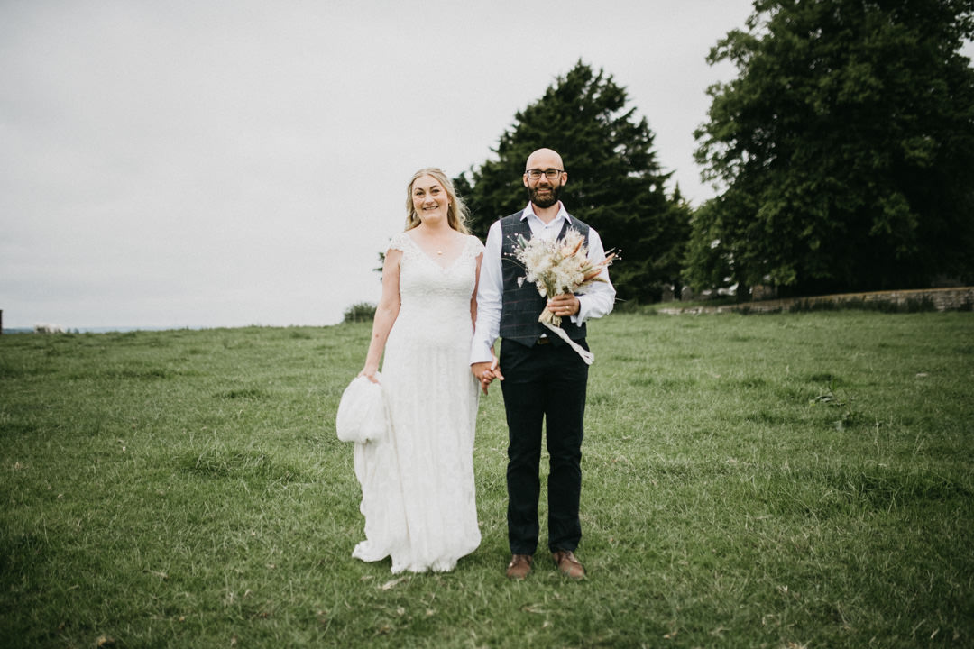 bride and groom stood in field holding wedding flowers