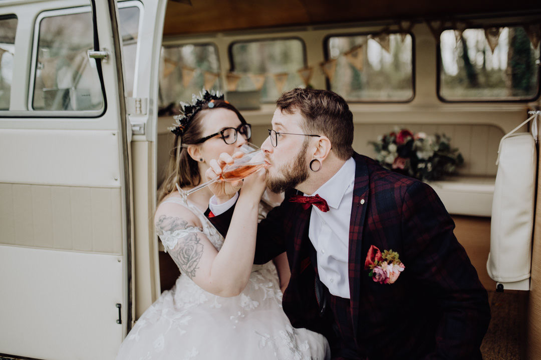 bride and groom sat in door of camper van drinking champagne