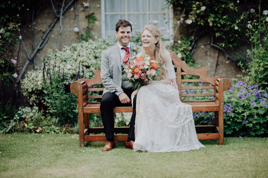 bride and groom sat on bench holding flowers