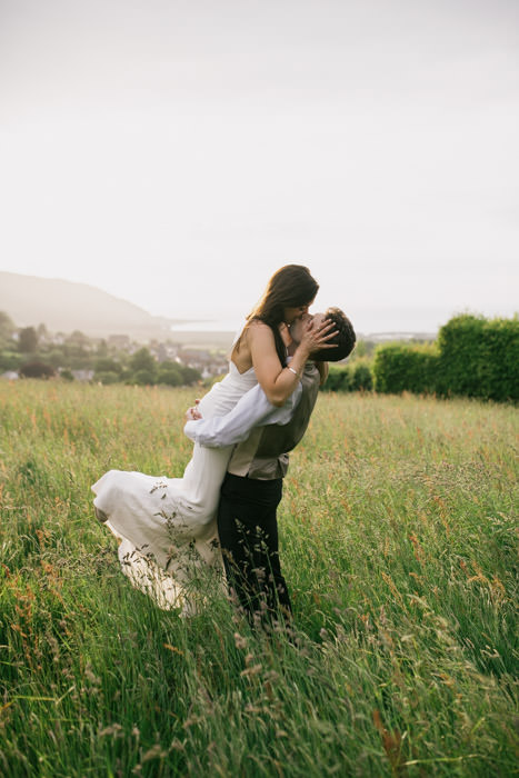 bride and groom kissing in meadow during sunset