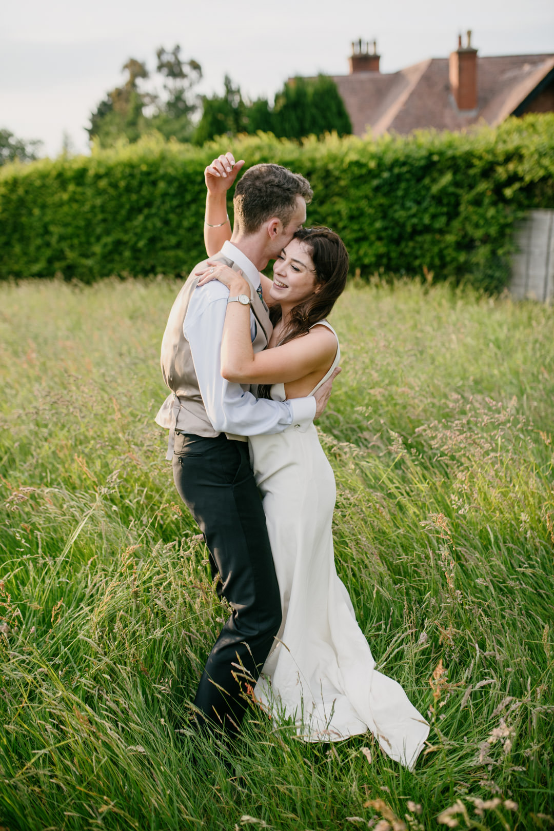 bride kissing husband in meadow at sunset