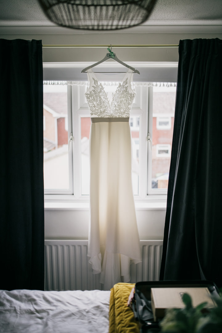 wedding dress hanging near large window in bedroom