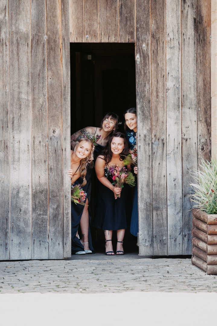 bridesmaids stood in large barn holding flowers