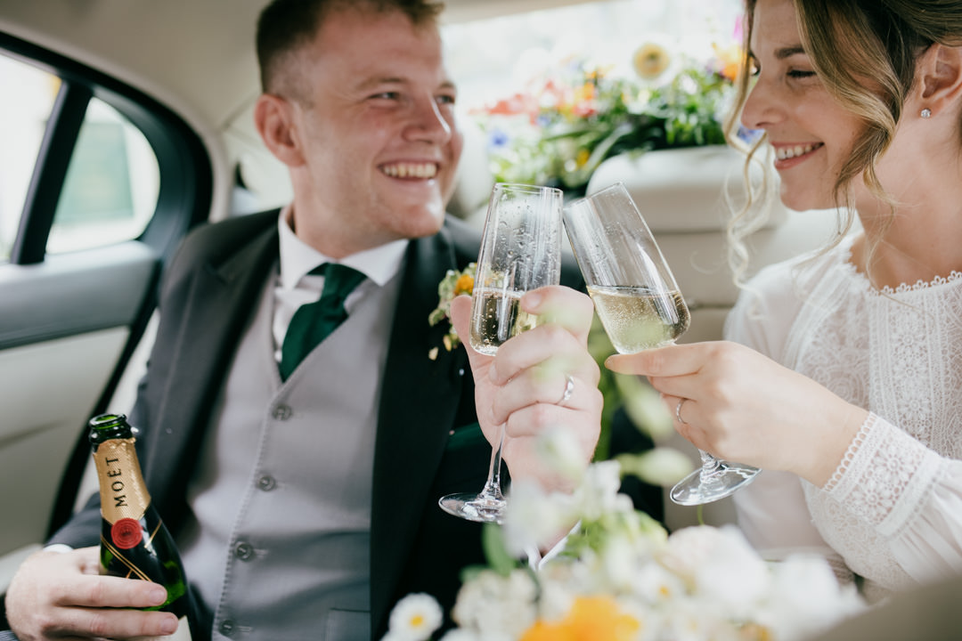 bride and groom drinking champagne in car