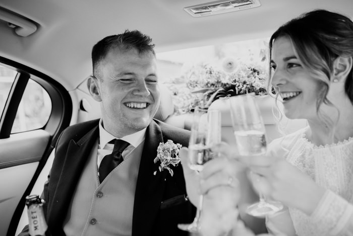 bride and groom sat in car drinking champagne