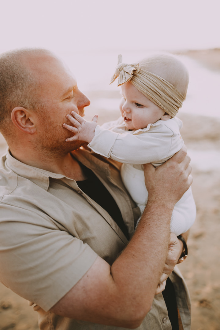 father holding baby girl on beach