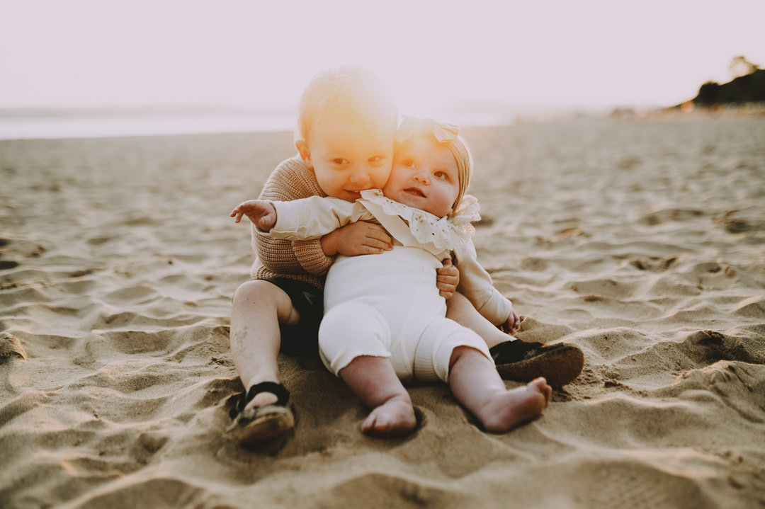 baby children sat on sandy beach during sunset