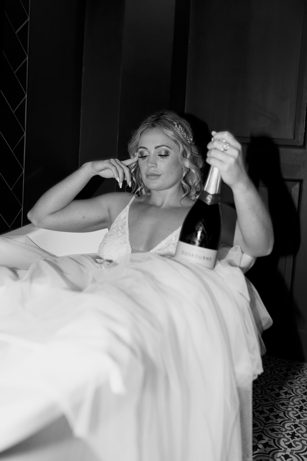 wedding bride in white dress laying bath tub drinking champagne