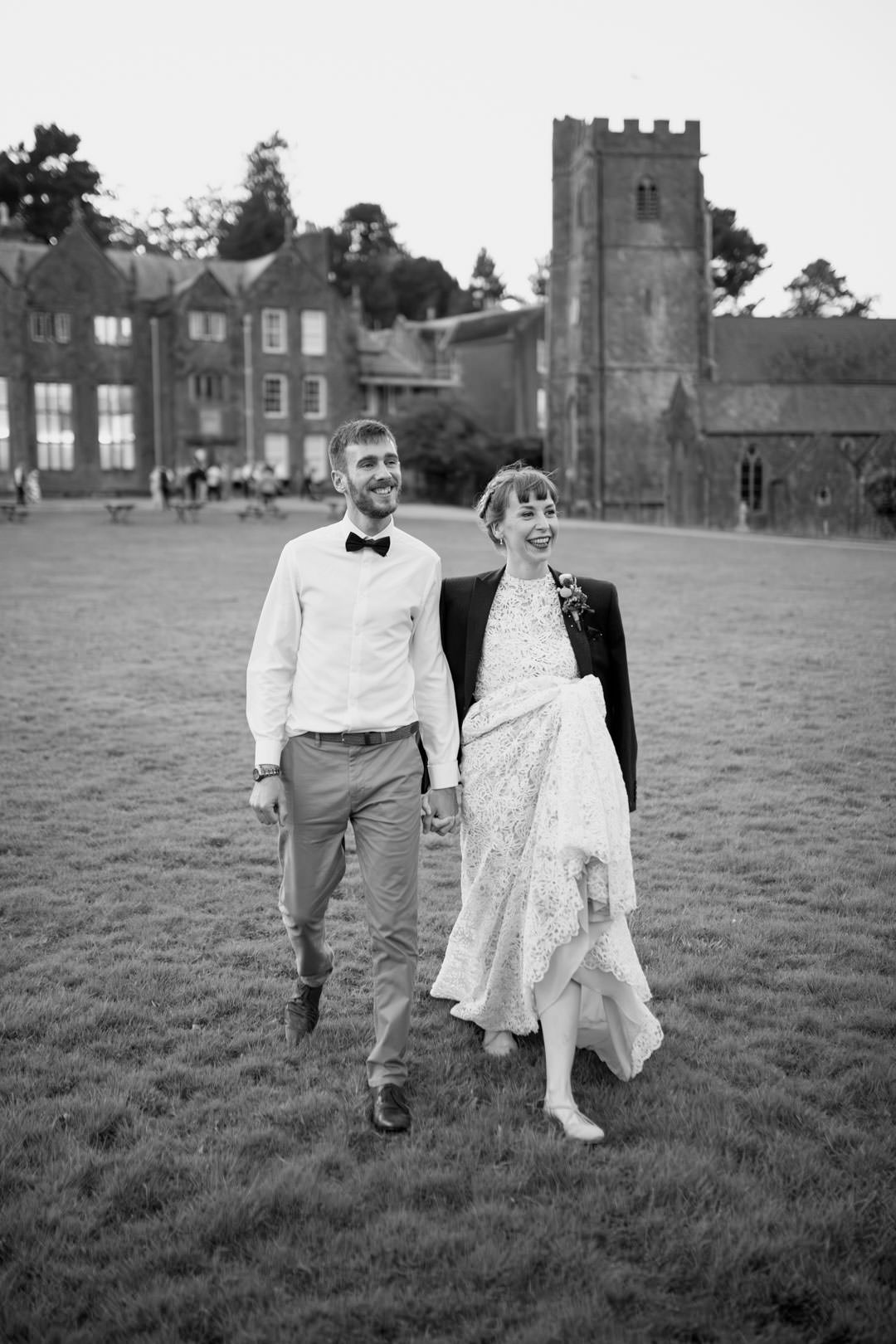 bride and groom walking hand in hand on lawn outside large manor house