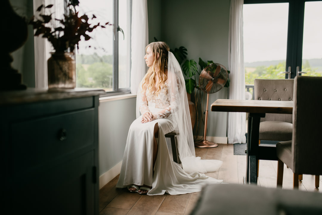 bride sat on stool in white dress near window