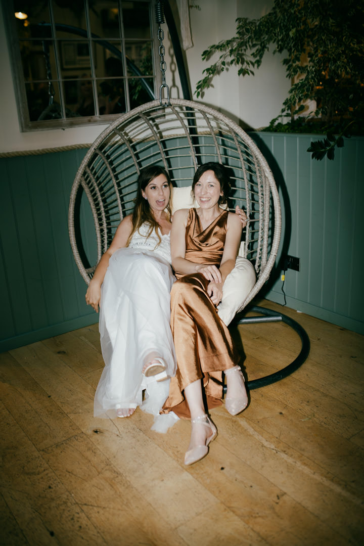 bride and bridesmaid sat in swinging chair laughing