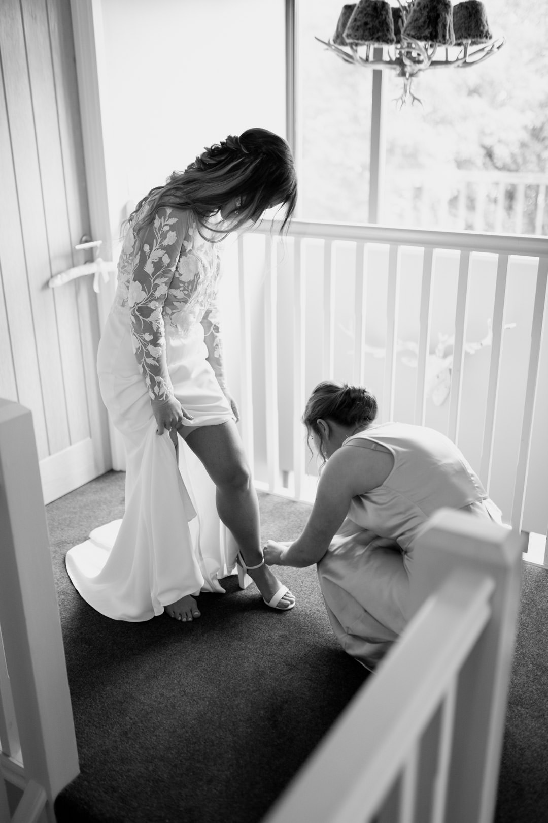 bride putting on shoes at top of large stair case in window light