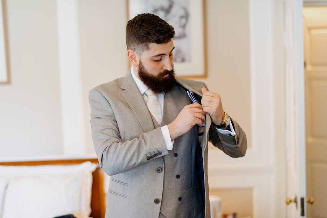 groom putting on jacket in large bedroom