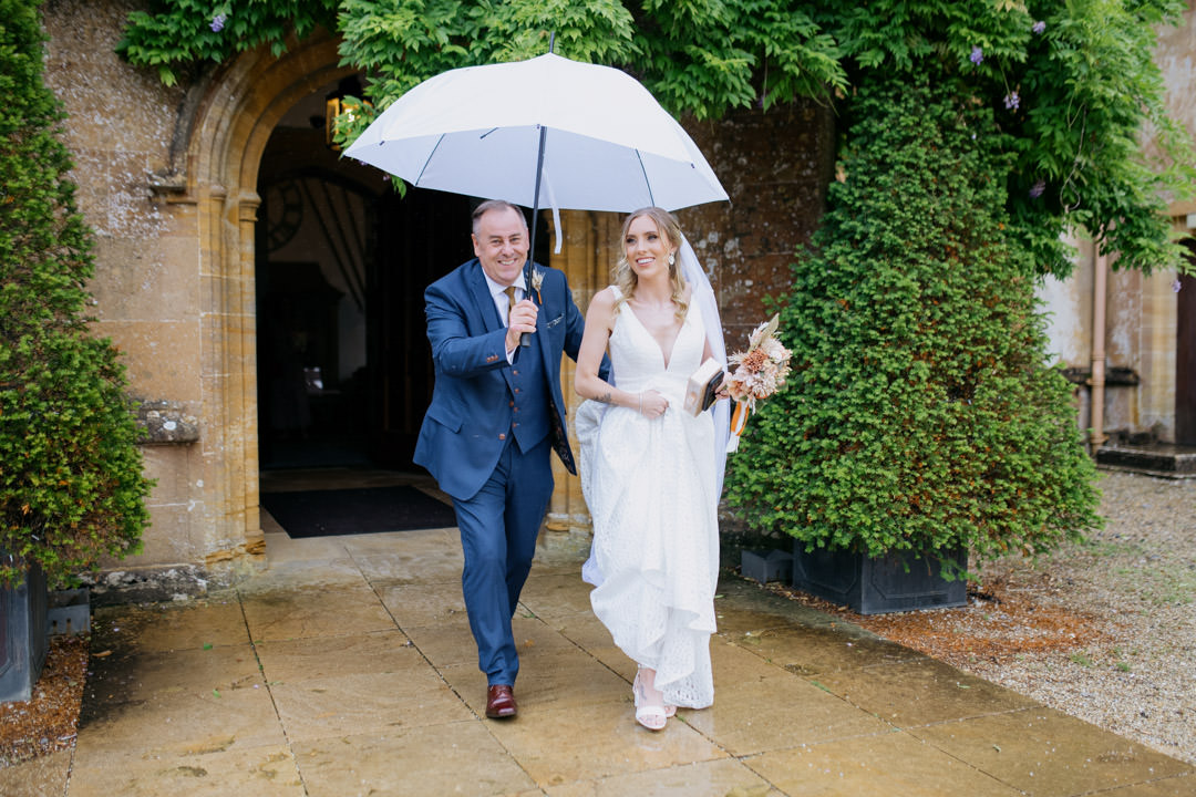 wedding bride walking with large white umbrella in rain