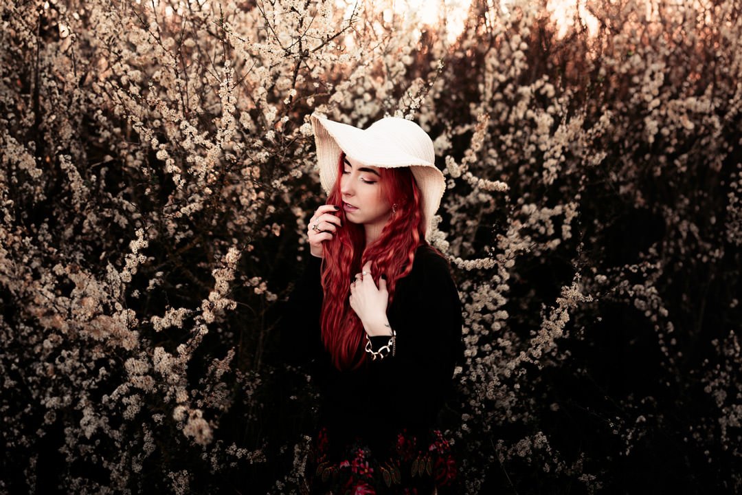 girl with red hair waring large hat under blossom tree
