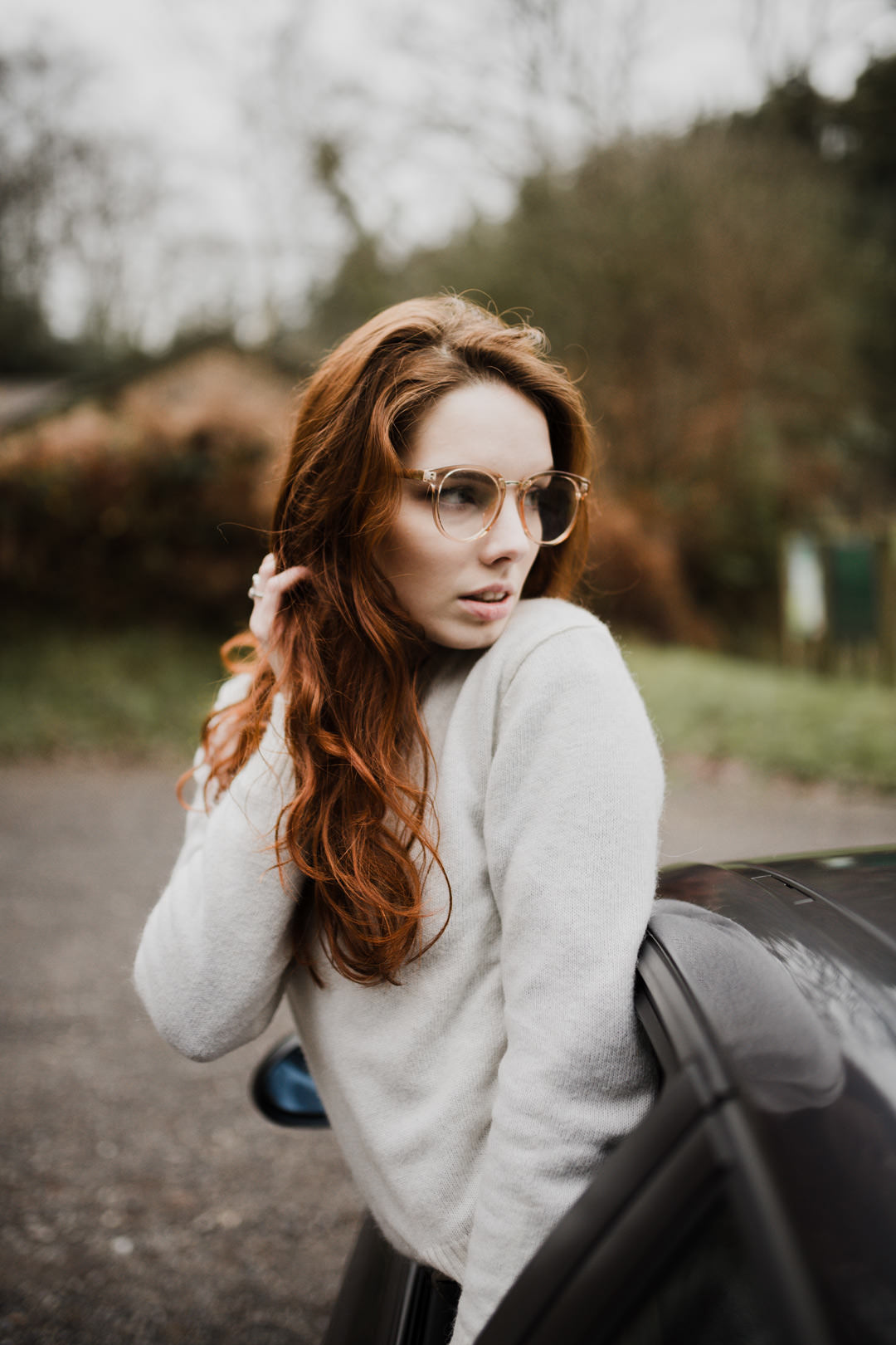 girl waring brown glasses leaning out of sports car