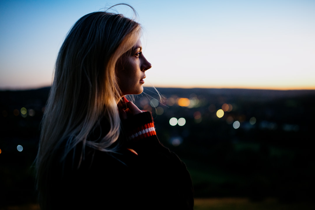 girl looking at city lights on top of hill at sunset