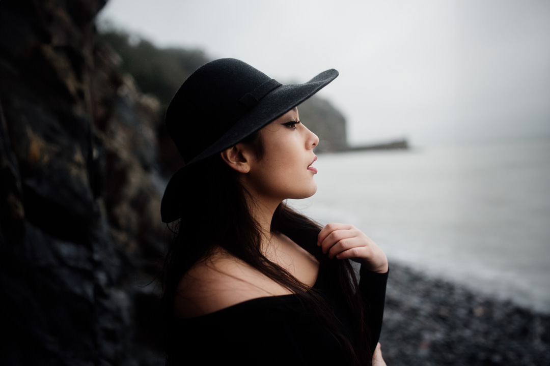 girl waring black hat stood on rocky beach next to ocean