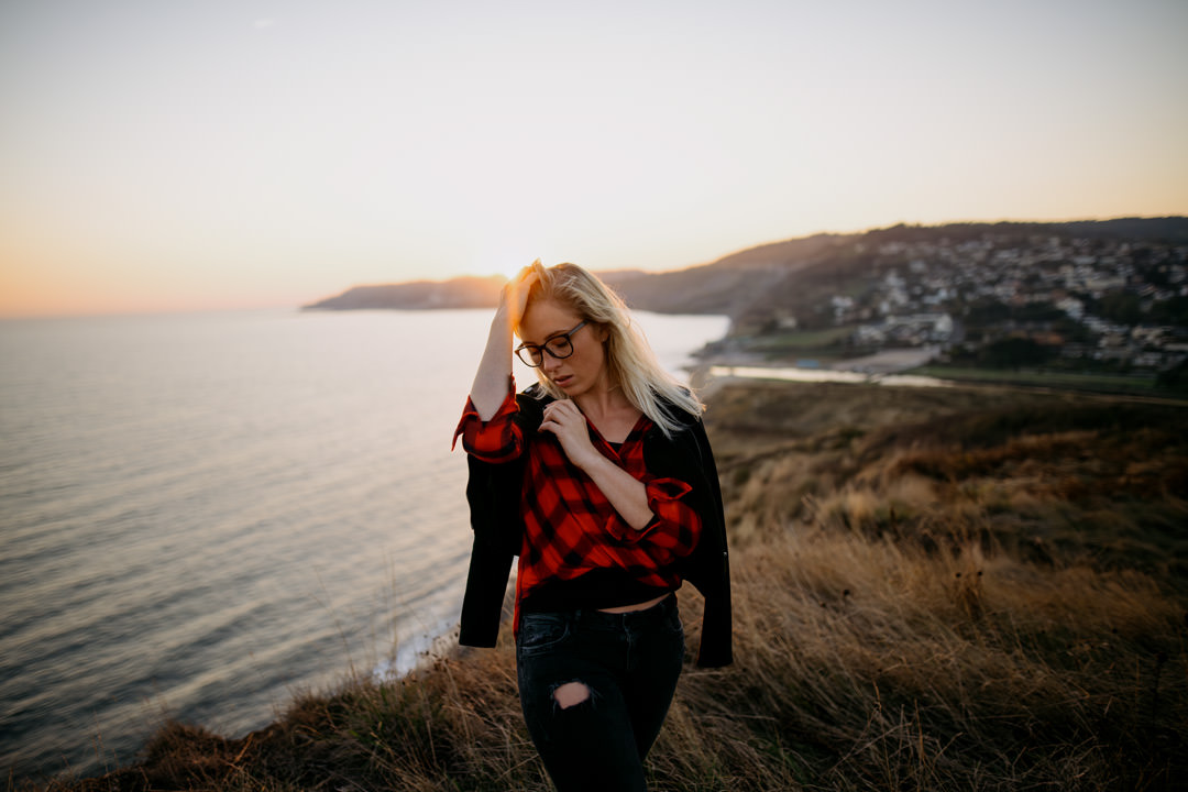 girl waring leather jacket stood on cliff top during sunset