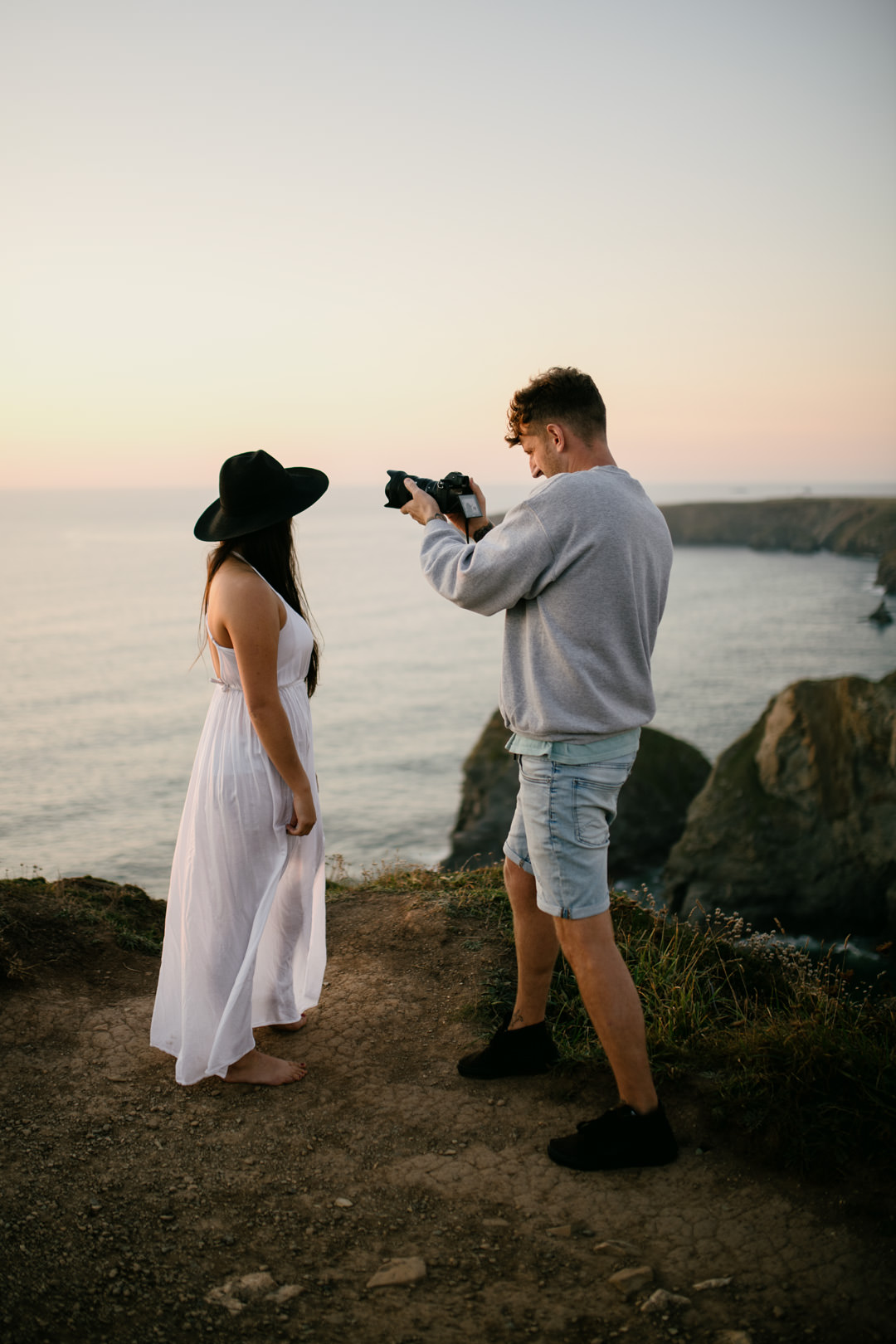 man takin photo of woman in white dress on cliff edge