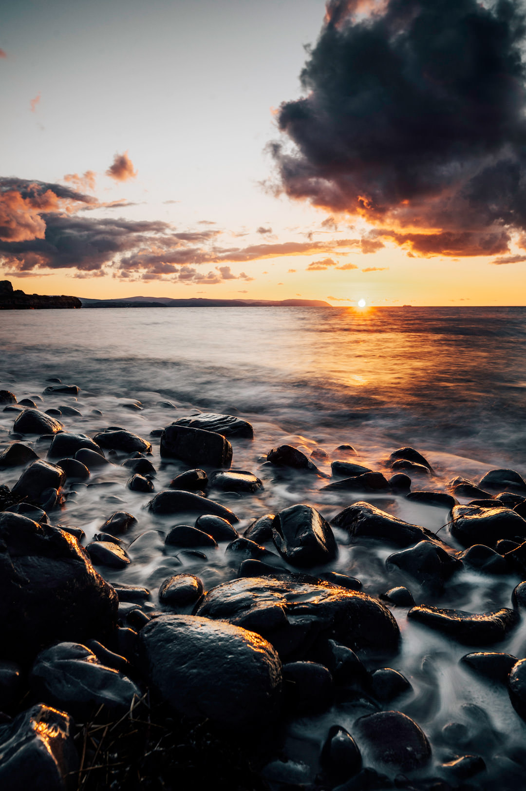 long exposure of rocks and ocean during orange sunset