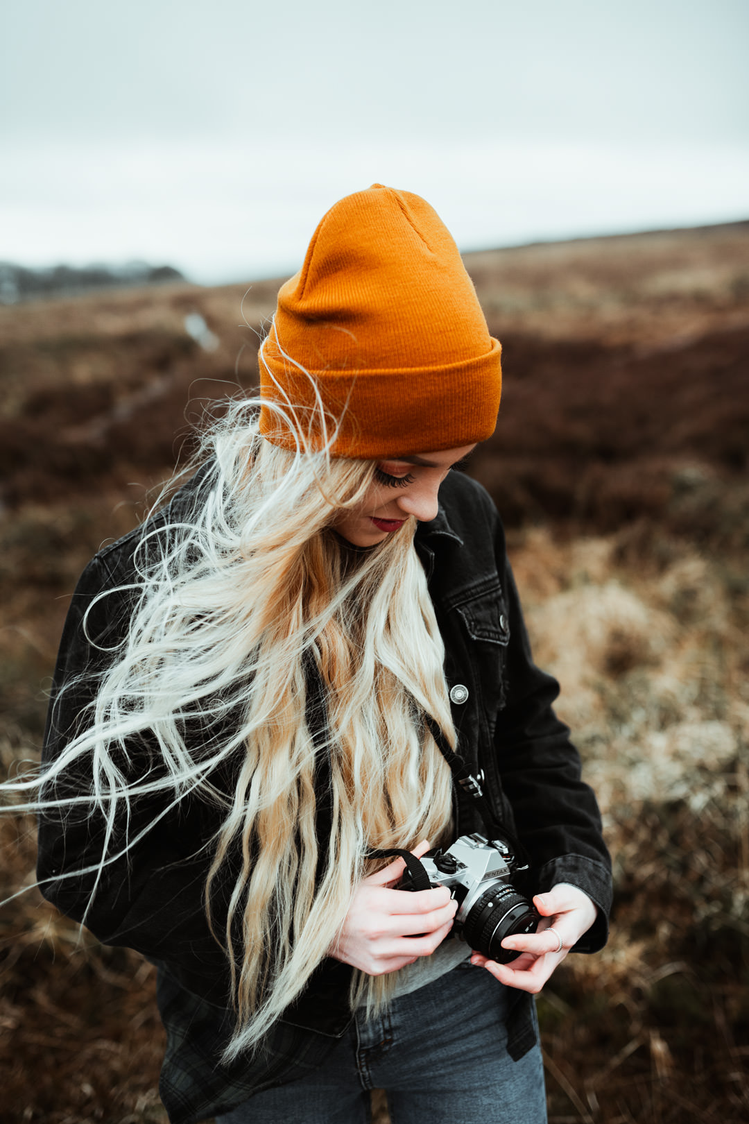 girl with blonde hair holding Nikon film camera in woods