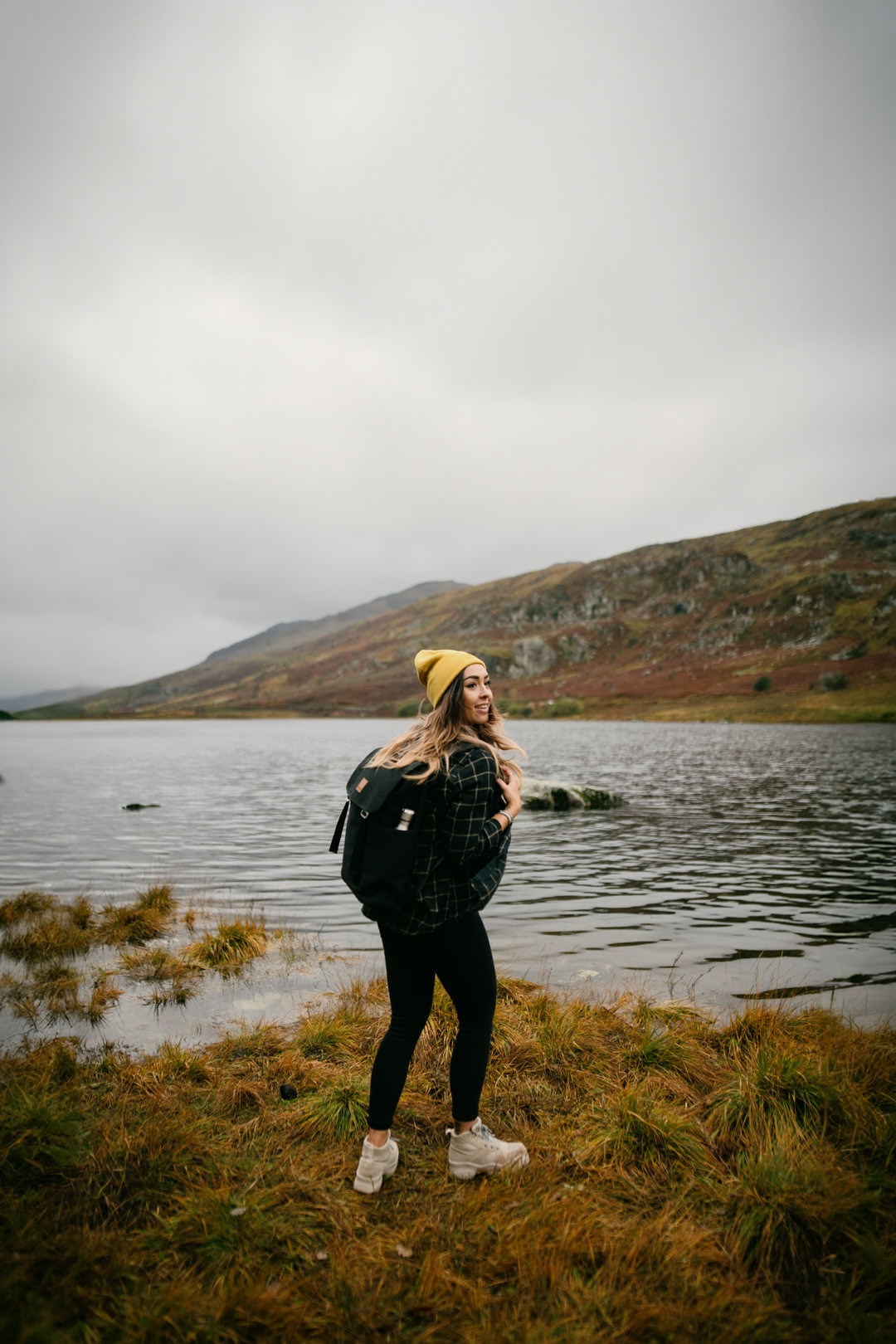 girl waring yellow beanie hat stood next to lake during cloudy day