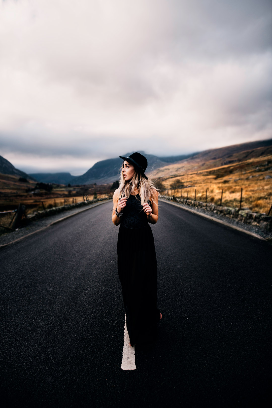 woman waring black dress in open road near large mountains