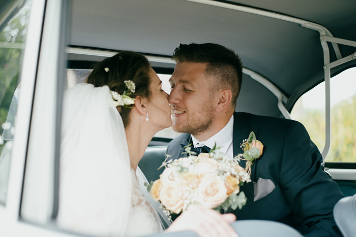 bride and groom sat in classic car kissing during daytime